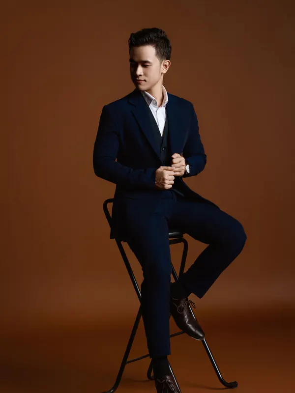 Jeune homme en costume bleu marine ajusté, assis sur un tabouret